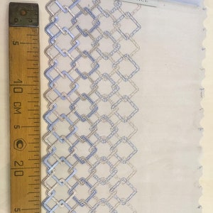 May include: A close-up of blue and silver embroidered lace trim with a geometric pattern. The trim is on a white background and a ruler is visible in the image. The label reads "Imperial Lace".