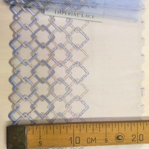 May include: A close-up of blue and silver lace trim with a geometric pattern. The lace is measured with a ruler showing 10 centimeters.