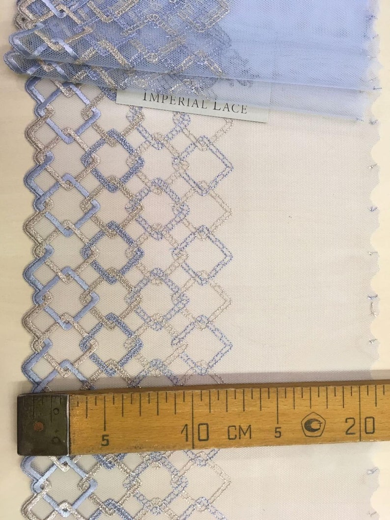May include: A close-up of blue and silver lace trim with a geometric pattern. The lace is measured with a ruler showing 10 centimeters.