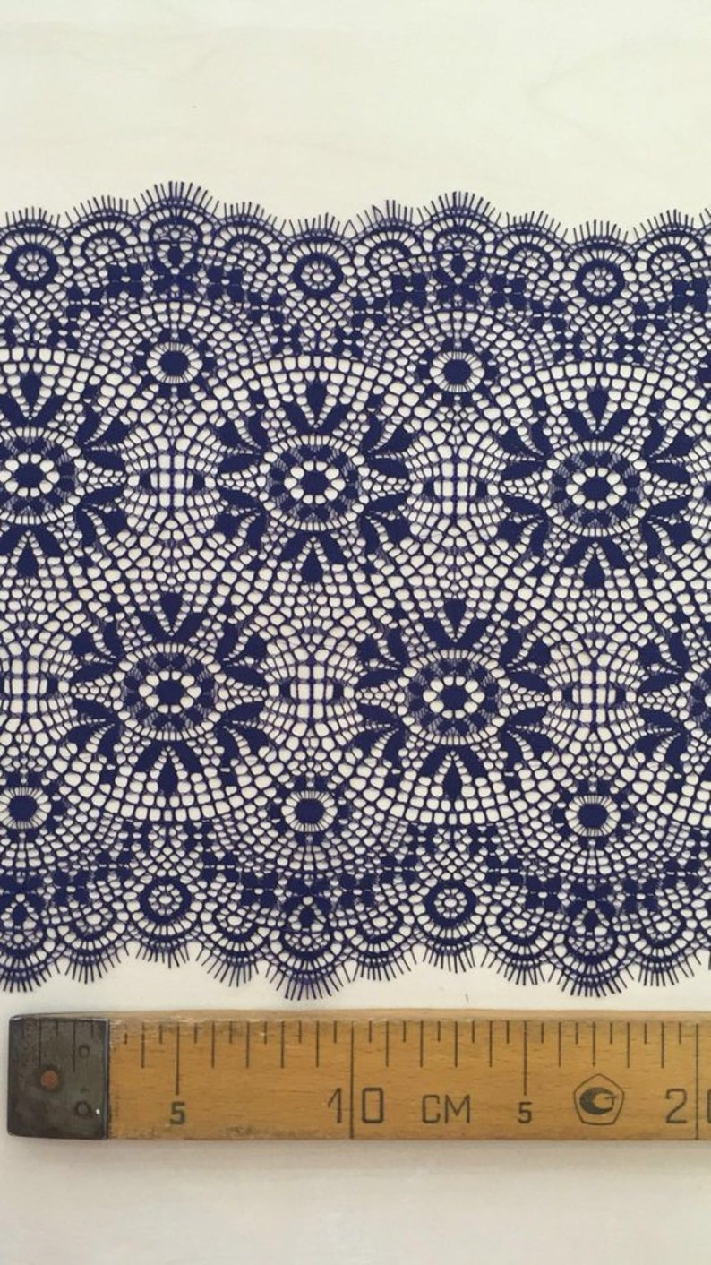 May include: A close-up of navy blue lace trim with a delicate, intricate pattern. The lace is shown next to a ruler measuring 10 centimeters.