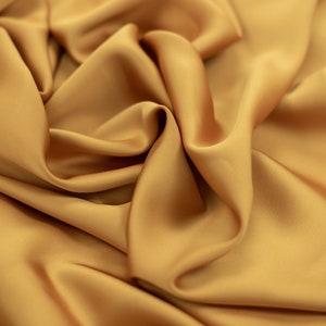 May include: A close-up of a smooth, golden fabric with soft folds and wrinkles. The fabric has a luxurious and elegant appearance.