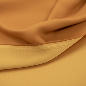 May include: Close-up of a fabric with two shades of brown. The fabric is folded over and stitched together. The top layer is a darker brown and the bottom layer is a lighter brown.