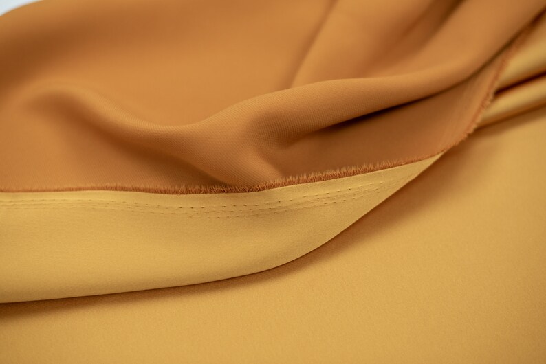 May include: Close-up of a fabric with two shades of brown. The fabric is folded over and stitched together. The top layer is a darker brown and the bottom layer is a lighter brown.