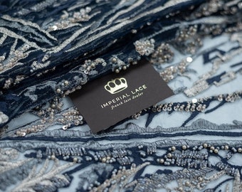 May include: Close-up of a navy blue and silver beaded lace fabric with a black tag that reads "Imperial Lace French Lace Dealer".