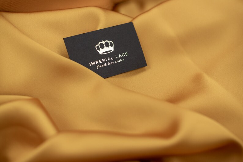 May include: A black business card with a white crown and the text "IMPERIAL LACE french lace dealer" on a gold fabric background.