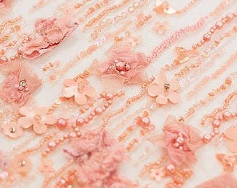 May include: Close-up of delicate pink fabric with beaded embellishments. The fabric features a floral design with small, intricate flowers and pearls.