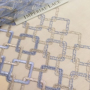 May include: A close-up of a light blue and gold geometric lace fabric. The fabric has a repeating pattern of squares and rectangles. The text "IMPERIAL LACE" is visible in the upper left corner of the image.