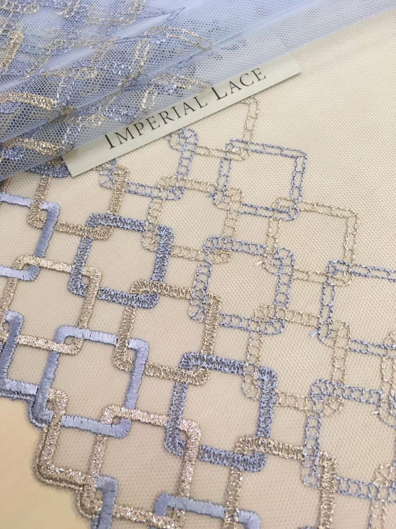 May include: A close-up of a light blue and gold geometric lace fabric. The fabric has a repeating pattern of squares and rectangles. The text "IMPERIAL LACE" is visible in the upper left corner of the image.