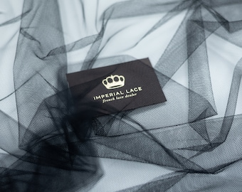Peut inclure: Une carte noire avec des lettres dorées qui disent "IMPERIAL LACE french lace dealer" et un logo de couronne dorée. La carte est posée sur un tissu de tulle noir.