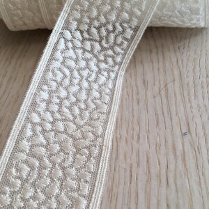 May include: White lace trim with a delicate floral pattern. The trim is approximately 1 inch wide and has a soft, flowing texture.