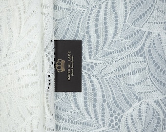 Könnte beinhalten: Weißer Spitzenstoff mit einem zarten Blumenmuster. Der Stoff ist über sich selbst gelegt und zeigt ein kleines schwarzes Etikett mit der Aufschrift "Imperial Lace, French lace dealer".