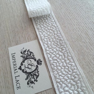 May include: White lace trim with a delicate, embossed pattern. The trim is folded in half and the label "IMPERIAL LACE" is visible.