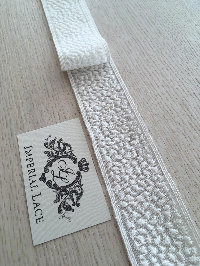 May include: White lace trim with a delicate, embossed pattern. The trim is folded in half and the label "IMPERIAL LACE" is visible.
