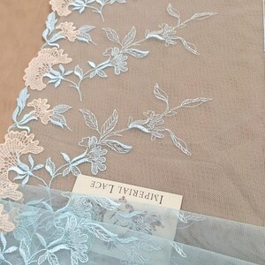 K&ouml;nnte beinhalten: Hellblaue und wei&szlig;e florale Spitzenstoff mit dem Text "Imperial Lace" auf einem wei&szlig;en Etikett.