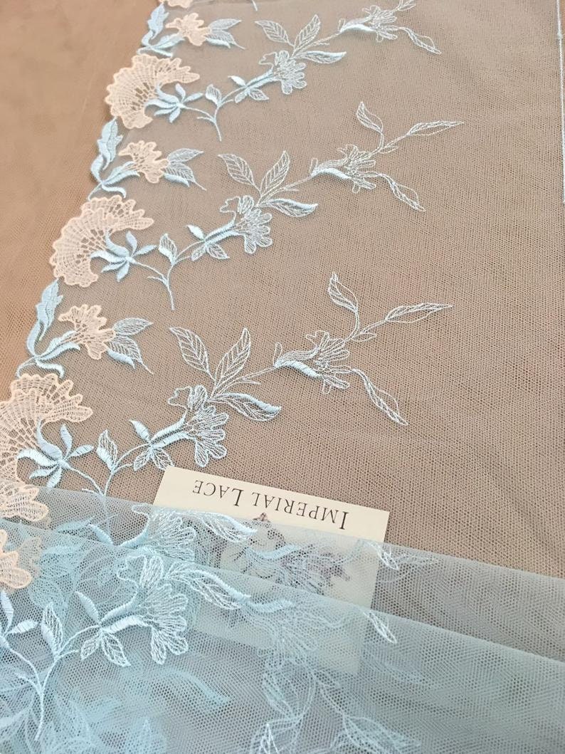 K&ouml;nnte beinhalten: Hellblaue und wei&szlig;e florale Spitzenstoff mit dem Text "Imperial Lace" auf einem wei&szlig;en Etikett.