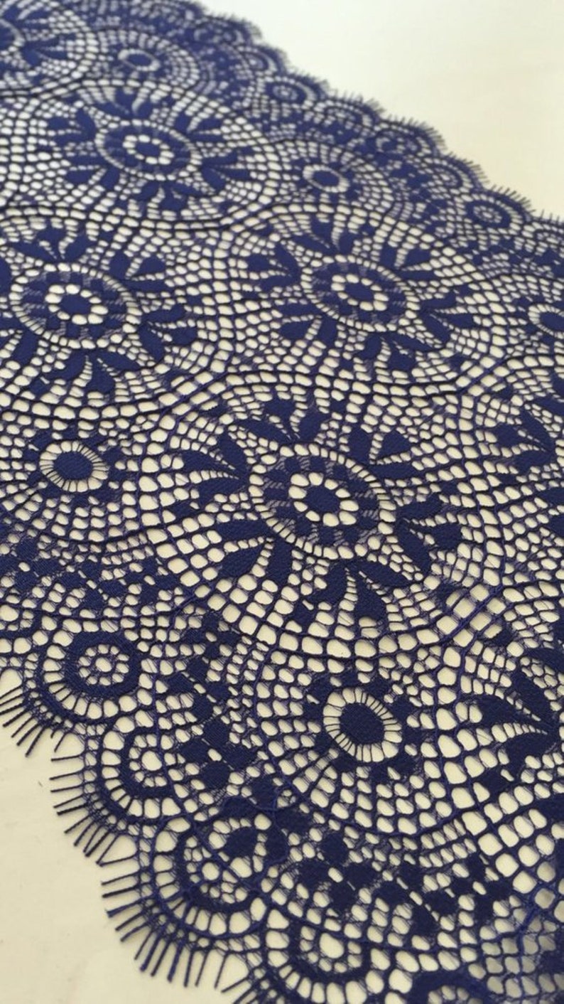 May include: Navy blue lace trim with a delicate floral pattern. The lace has a scalloped edge and is perfect for adding a touch of elegance to any project.