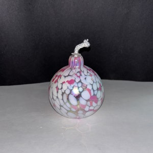 May include: A white and pink glass oil lamp with a white wick. The lamp is round and has a speckled pattern.