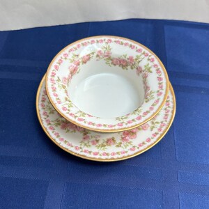 May include: A set of two white porcelain bowls with a pink floral pattern and gold trim. The bowls are nested together.