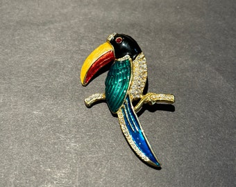 May include: A gold-tone toucan brooch with a black head, yellow beak, red accents, and blue and green wings. The toucan is adorned with clear rhinestones.