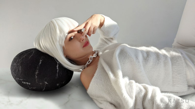 A girl with white hair is lying on a black felted stone pillow.