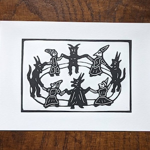 以下が含まれることがあります： 7人の人物が輪になって手をつなぎ、踊っている白黒の木版画。人物は様式化されており、角、尻尾、とがった帽子をかぶっている。