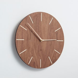 Side look at the wood mid century modern wall clock. Made of light wood indexes and painted to similar colour clock hands are clearly visible on the  dark clock face. It is easy to read the time even from the distance. Clock is simple and elegant.