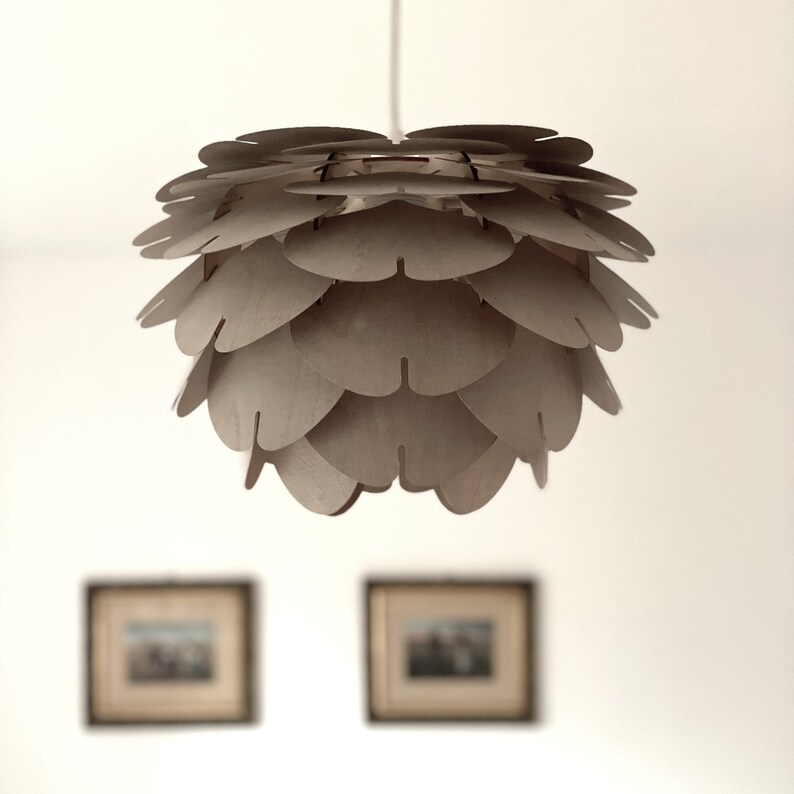 Pendant light made of translucent wood. Brown colour. Mid century modern style lamp hanging in a room with pictures on the wall.