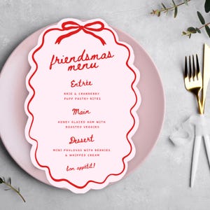 May include: A Friendsmas menu card with a red scalloped border and bow design, placed on a pink plate. The menu lists Entrée, Main, and Dessert courses, including Brie & Cranberry Puff Pastry Bites and Honey Glazed Ham with Roasted Veggies.