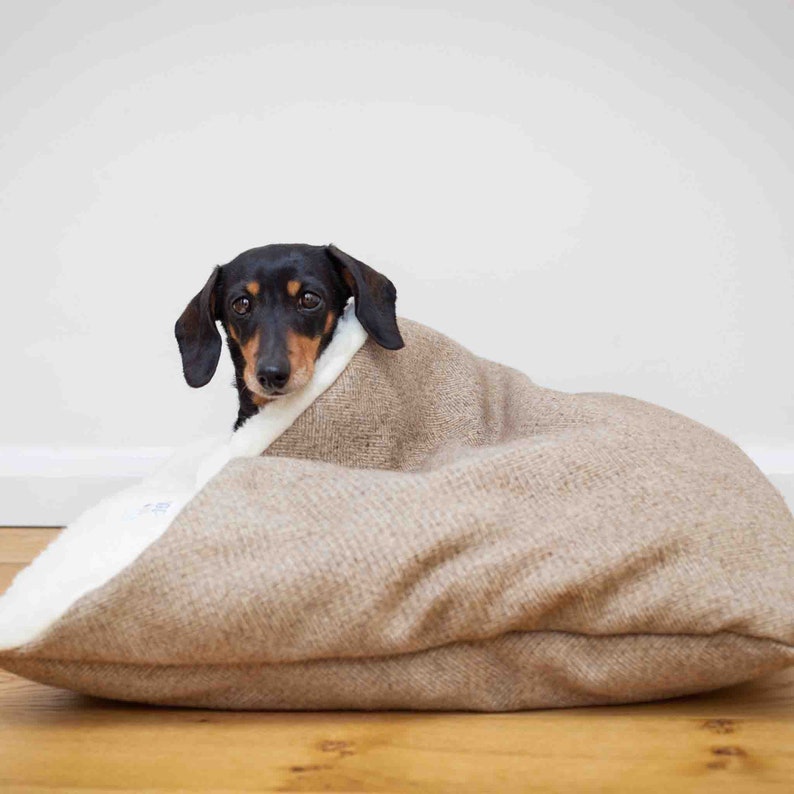 miniature dachshund dog sat in handmade doggy den / cave bed. envelope opening. stone brown herringbone tweed outer lined with cream faux sheepskin. machine washable cover. memory foam and orthopaedic foam crumb inner cushion.