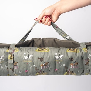 May include: A green and brown equestrian-themed yoga mat with a carrying strap. The mat features a repeating pattern of horses and riders, saddles, and jumps.