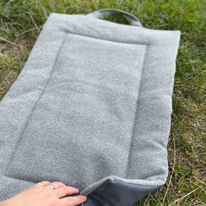 dog picnic pad/ travel mat in pewter grey herringbone tweed fabric laid out on the grass. matching straps and handles, waterproof backing and lined with wadding for comfort.