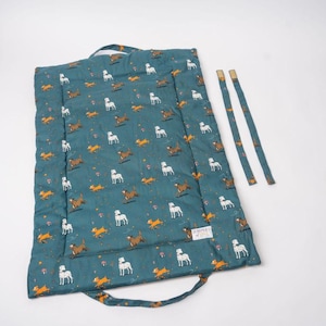 May include: A teal blue play mat with a pattern of white and brown dogs and foxes. The mat has two fabric handles and comes with two long teal blue straps.