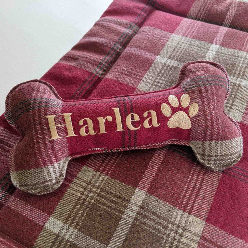 Handmade red tartan dog bone toy, personalised named embroidery in gold thread and pawprint icon. matching red tartan crate mat.