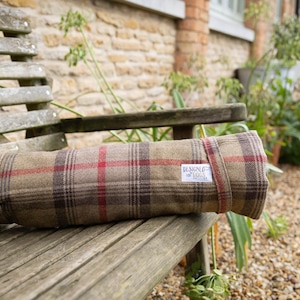 Può includere: Una coperta di lana a quadri arrotolata con un'etichetta bianca che dice "Design by Laura". La coperta è su una panca di legno.