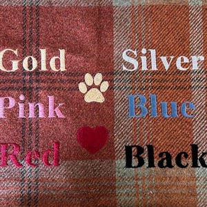 May include: A red and brown plaid fabric with embroidered words in different colors. The words are "Gold", "Pink", "Red", "Silver", "Blue", and "Black". There is a paw print and a heart embroidered on the fabric.