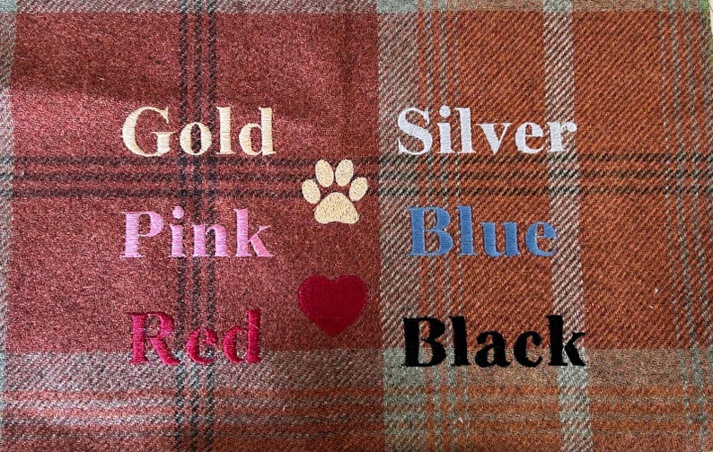 May include: A red and brown plaid fabric with embroidered words in different colors. The words are "Gold", "Pink", "Red", "Silver", "Blue", and "Black". There is a paw print and a heart embroidered on the fabric.