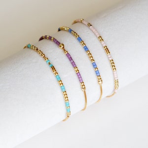 May include: Four gold beaded bracelets with adjustable sliding knots. The bracelets feature different color combinations of turquoise, purple, blue, and pink beads.