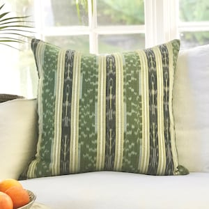 May include: A green and cream striped throw pillow with a subtle ikat pattern. The pillow is on a white sofa with a white throw pillow beside it.