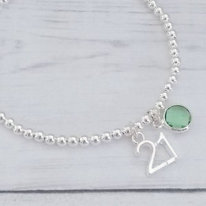 May include: A silver beaded bracelet with a silver charm that says "21" and a green gemstone charm.