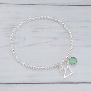May include: A silver beaded bracelet with a silver charm that says "21" and a green gemstone charm.