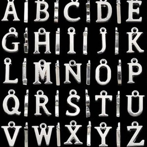 May include: A set of 26 silver metal alphabet letter charms. Each letter is individually attached to a jump ring. The letters are all uppercase and are arranged in alphabetical order.