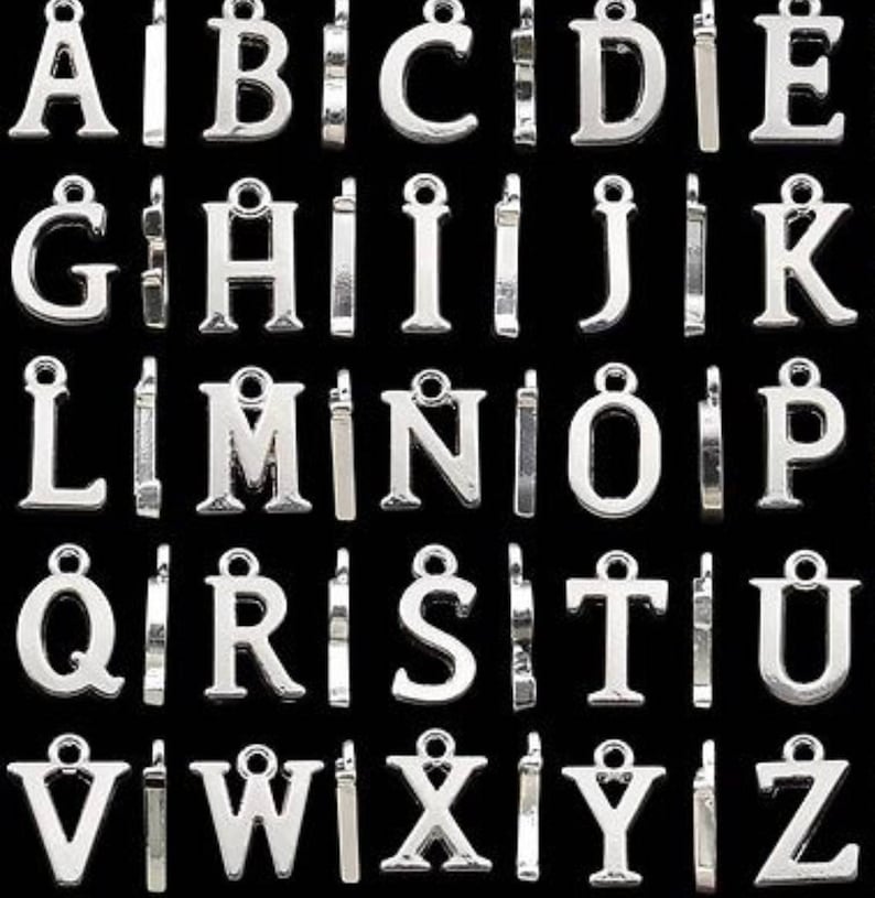 May include: A set of 26 silver metal alphabet letter charms. Each letter is individually attached to a jump ring. The letters are all uppercase and are arranged in alphabetical order.
