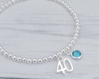 May include: A silver beaded bracelet with a charm that says "40" and a light blue gemstone.
