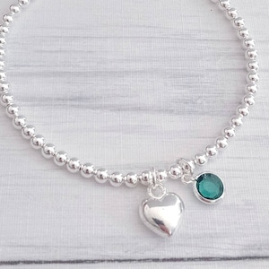 May include: A silver beaded bracelet with a heart charm and a green gemstone charm.