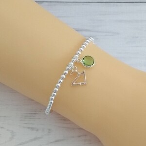 May include: A silver beaded bracelet with a green gemstone charm and a silver charm with the number 21.
