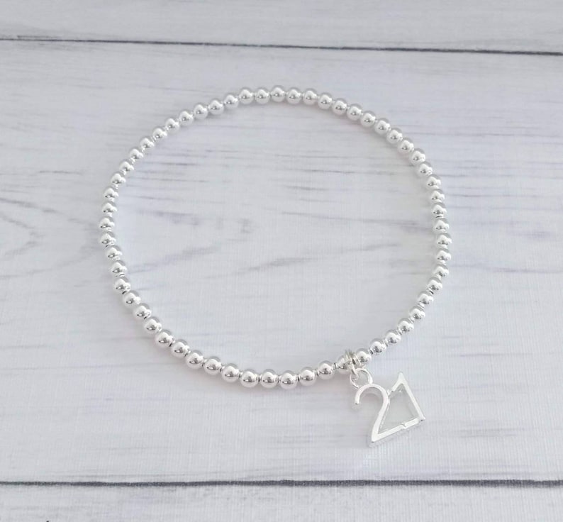 May include: A silver beaded bracelet with a silver charm that says "21".