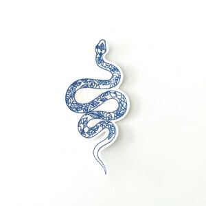 May include: An iron-on patch embroidered in blue, depicting a snake with floral details.