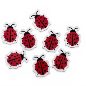 May include: Eight red ladybug patches with black spots and antennae are displayed. Each patch has a white border, providing a contrasting outline against the white background. These patches are suitable for fabric crafts.