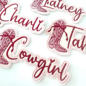 May include: Five pink and white embroidered iron-on patches with a pink cowboy boot design and names "Charli", "Lainey", "Tahlia", "Cowgirl" and a heart.