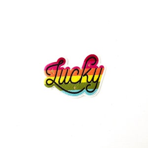 May include: Rainbow-colored embroidered patch with the word "Lucky" in black cursive lettering.